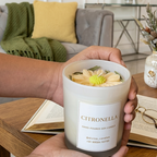 Hand holding a citronella candle with a living room in the background